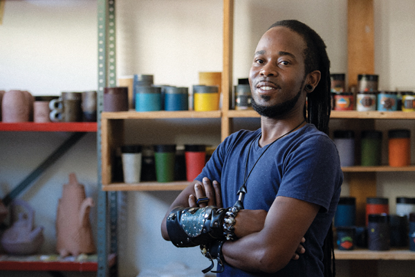 11 Sandile Brian Cele standing in his studio in front of a collection of cups and mugs.