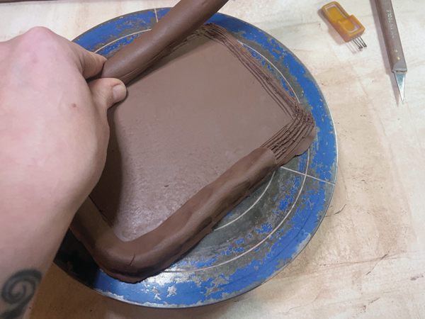 3 Using a thumb and index finger, press a coil along the edge of the scored base. Begin an inch from the corner.