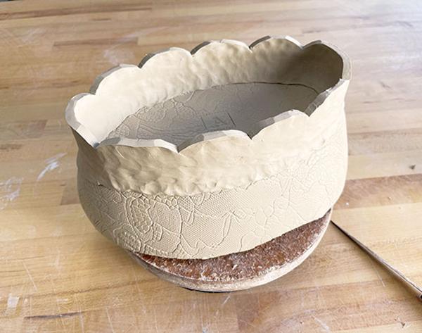 7 After pinching up the coil to create a foot, use a fettling knife to cut a scalloped edge on the rim.
