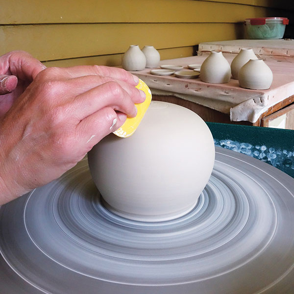 3 Compress the exterior with a rubber rib. Use the tip of a wooden rib to remove excess clay from the base.