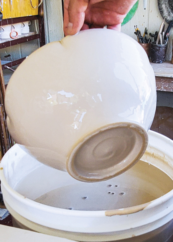 12 After submerging the bowl only up to the rim to prevent the slip from getting inside, remove the bowl from the bucket, tilt it at an angle, and let all the excess slip drip off the bottom.