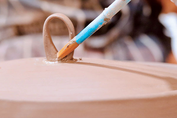 13 For the lid, score the handle end and attachment area, add slip, then attach the handle in the center of the dome. Use a damp brush to refine all of the handle attachments.