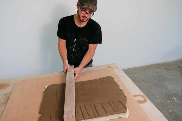 Attaching a grogged stoneware slab to the back of the colored porcelain using a board prior to rolling the slab out to its final thickness.