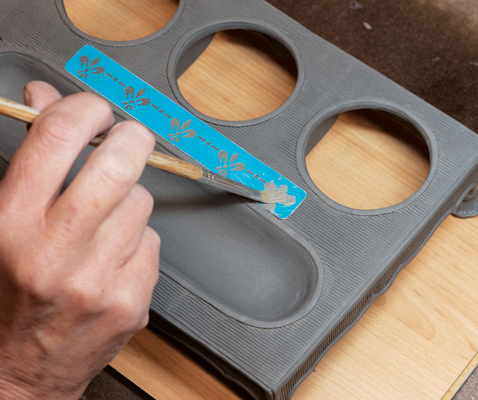 18 Decorate the top of the piece by painting over a stencil with thick slip in the color of your choice. 