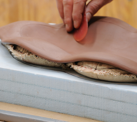 3 Trim a slab to the size of the template. Place it so that the clay edge lines up with the cloth. Rib the slab into the mold.