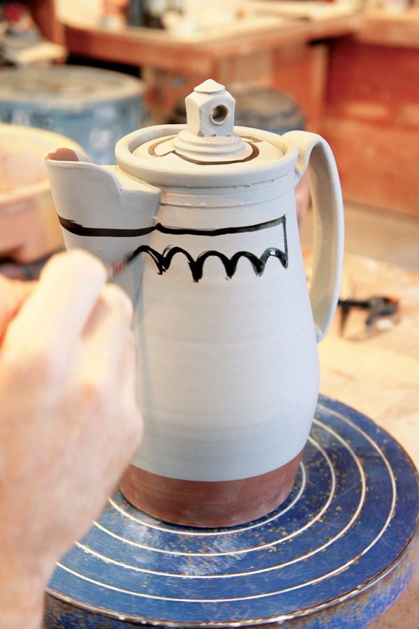 8 Apply white slip, place the pitcher on a banding wheel, then draw shapes with sumi ink.