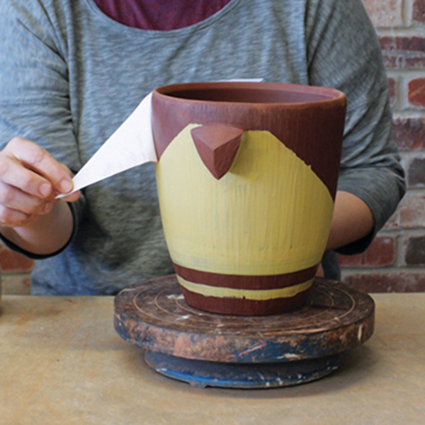 4 Apply paper stencils and a colored slip. Once the slip is no longer tacky, remove the stencil.
