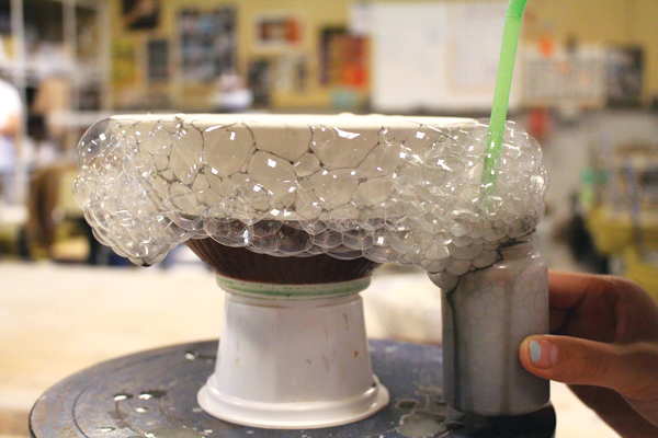 2 Add dish soap to the glaze and slowly blow through a straw into the glaze container to create bubbles that go onto the piece. Slowly spin the banding wheel to apply the bubble glaze evenly.