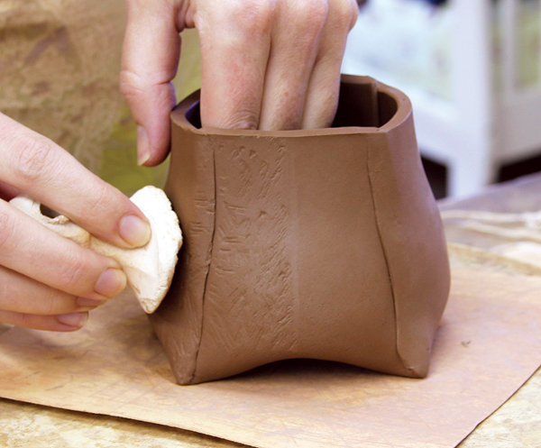 6 I push a carved bisque stamp into the outside surface of the pot, while holding one hand on the inside of the pot.