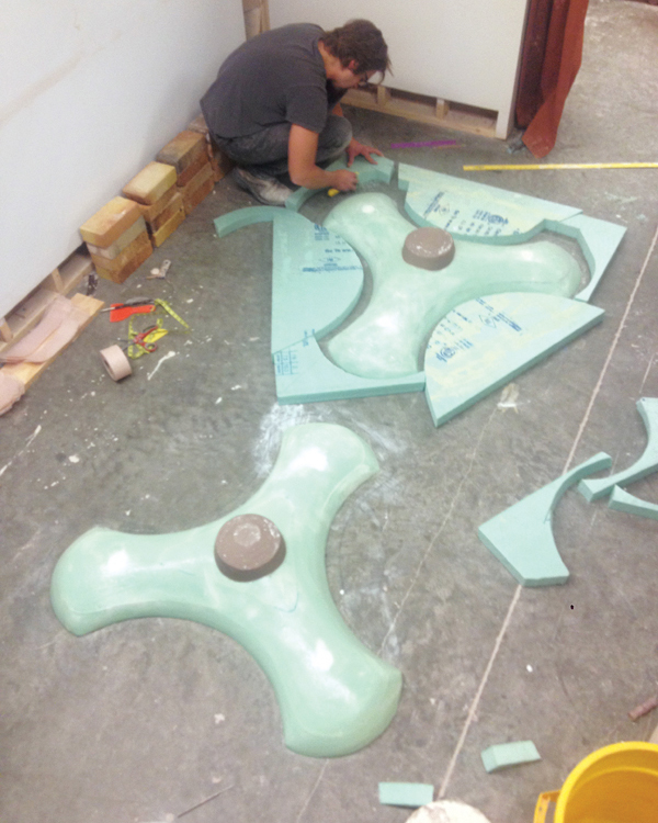 5 Foam cottles are set up around each tiller form in preparation for casting it in plaster. Clay coils seal the join between the foam and the floor to prevent plaster from escaping. Bricks are used to weight down the foam so it stays in place during the process. Plaster is poured over the model, and additional plaster is mounded on top as it sets up.