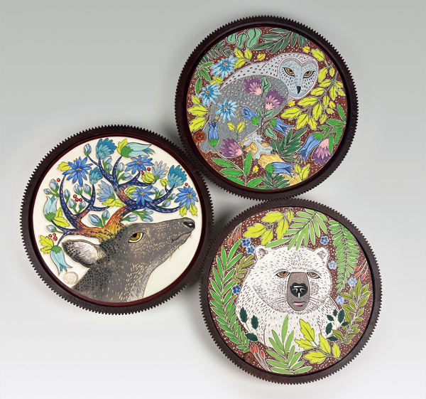 Clockwise from the left: Foraging in the Flower Garden (deer), Laguna Clay B Mix, fired in an electric kiln to cone 6, 2022; Forest Guardian (owl), Highwater Clays Earthen Red, fired in an electric kiln to cone 5, 2022; Forget Me Not (polar bear), Highwater Clays Earthen Red, fired in an electric kiln to cone 5, 2021. All tiles: 15½ in. (39 cm) in diameter, handbuilt, underglazes, sgraffito, slip trailing, selectively glazed, mounted in salvaged cast-iron gears, finished with Liquid Quartz. 