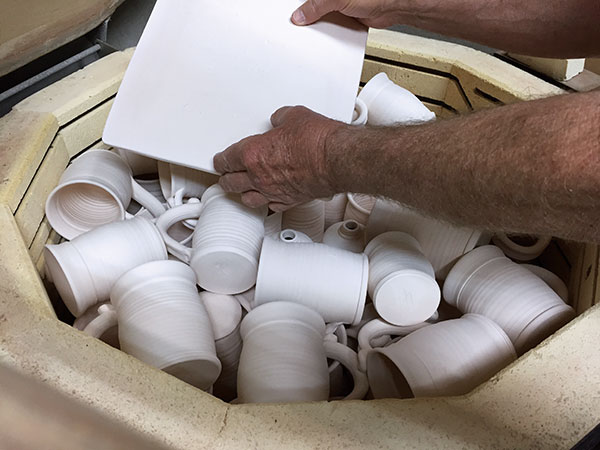 2 Square plate placed on top of tumble-stacked mugs, which are placed sideways on top of tumblers and lotion bottles standing upright.