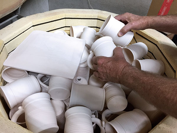 3 Tumble-stacked mugs placed sideways on top of tumblers and lotion bottles, with square plates on top.
