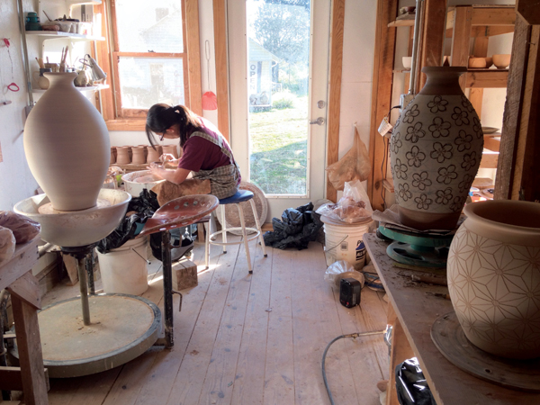  5 Hitomi Shibata throwing cups in the studio, framed by two slip-decorated jars with sgraffito decoration and a jar awaiting decoration.