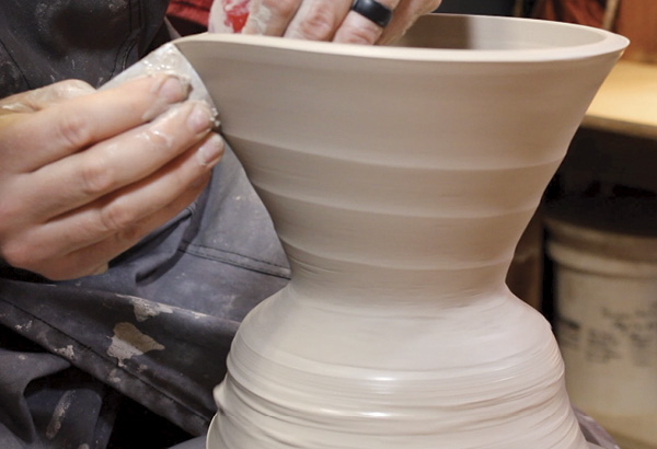 2 Slowing the wheel down, gently press a metal rib on the exterior wall, while in your left hand, press a soft silicone rib on the interior curve. Slowly draw both ribs up at the same time, capturing a slow spiral on the exterior surface as the wheel.