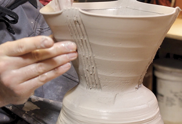 4 After carving your series of vertical lines, while the pot is still attached to the hump, gently fold the clay walls in between the furrows by pinching the clay on the exterior with your right thumb and first finger, while your left middle fingers.