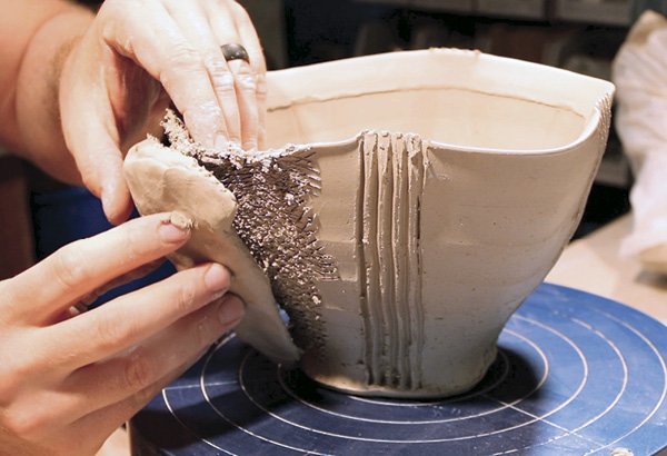 9 Using about a half pound of clay, pinch a wedge with a broad base and narrow tip. Flip the wedge upside down, score the interior portion, and begin attaching it to the side of the bowl you are working on.