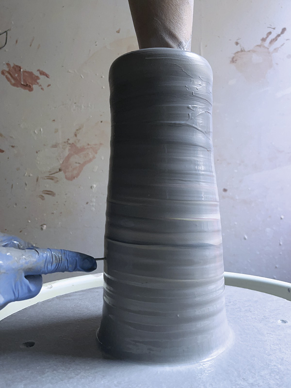 12 Throw a thick cylinder, accounting for the clay removed by the cheese slicer. Use a pin tool to ensure the wall thickness is even by sticking it through the wall until it hits your finger at various pointing the cylinder.