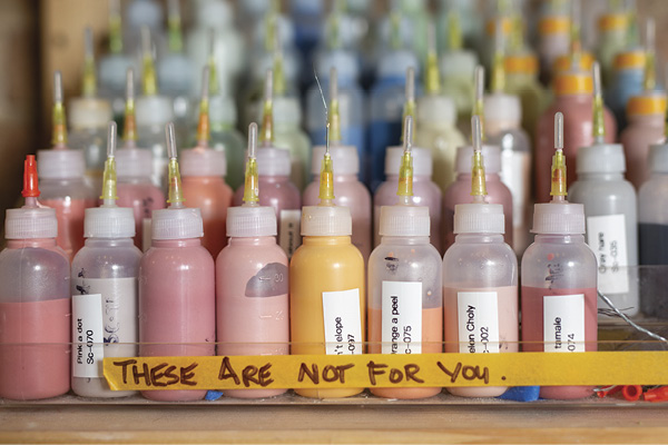 A shelf full of small glaze bottles.