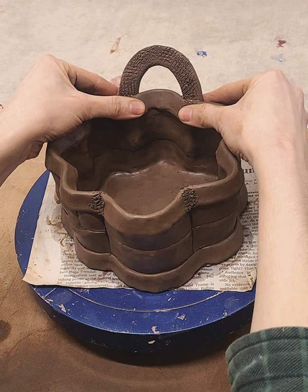 12 Mark the handle location on the top rim of your basket, and score and attach one to the exterior and one to the interior, sandwiching the wall in between. Repeat on the opposite side.
