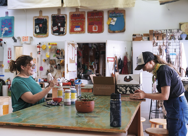 4 Two studio members, working at different stages of the making process, work together at a handbuilding table.