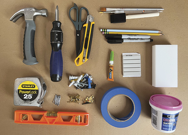 Clockwise from top left: hammer, ratcheting screwdriver with Phillips-head bit, scissors, utility knife, brushes, pencils, permanent markers, super glue, poster tack, melamine sponge, spackle, painter’s tape, assorted hardware, level, & tape measure.