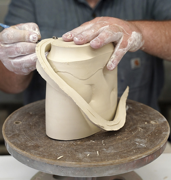 4 Flip the cylinder over, and using a hooked trimming tool, remove the excess clay at the bottom and foot in an expressive way, paying attention to the width of each cut.