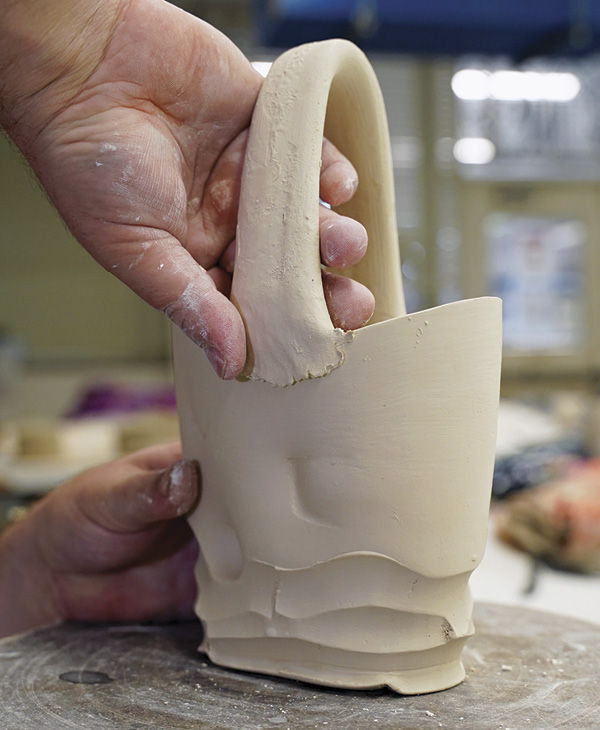 11 Slip and score the roughed-in handle and attach it to the rim of the form. Blend the interior surface flush and allow the excess material to protrude from the exterior surface. This will aid in shaping later.
