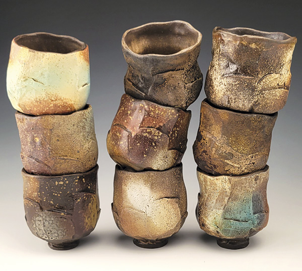 1 A collection of yunomis made with mid-fired black clay, wheel thrown, faceted, each yunomi treated with a different combination of variables to create different surface effects from the same firing, 2023.