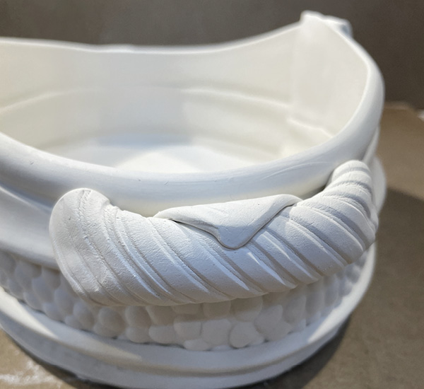 A6 Score and slip the vessel and add slip to the scored disks inside the croissant handle and attach to the vessel.