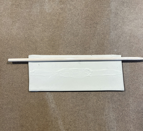 B2 Brush slip in the center along the length of the rectangle. Place a dowel along long edge and curve the clay around it.