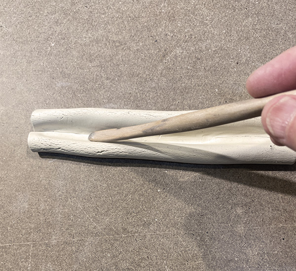 B4 Press the rounded end of a tool along the center to attach the edges of the tubular shapes to the center of the clay.