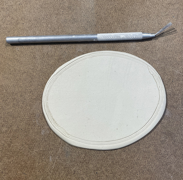 D2 Turn the clay piece over. Score its outer edge without making the edge ragged, then add slip.