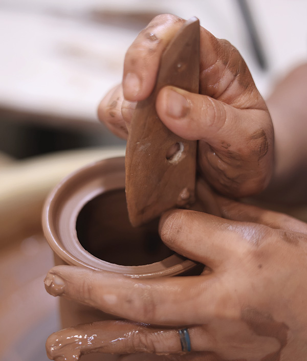 3 Wet the rim and a wooden rib. Use the right angle on the rib to push clay downward, creating a gallery.