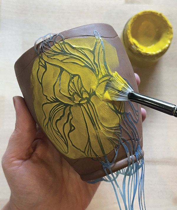 2 Apply a thin layer of underglaze over your stencil to create a base layer and further seal the stencil to the vessel.