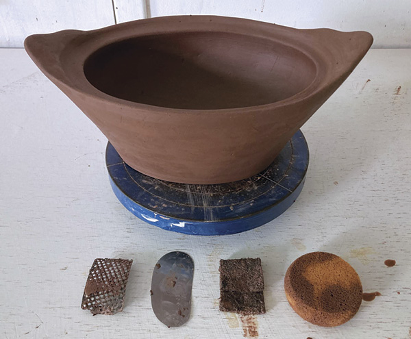12 Once leather hard, use a Surform, metal rib, scouring pad, and sponge to shape the exterior, foot, and handles.