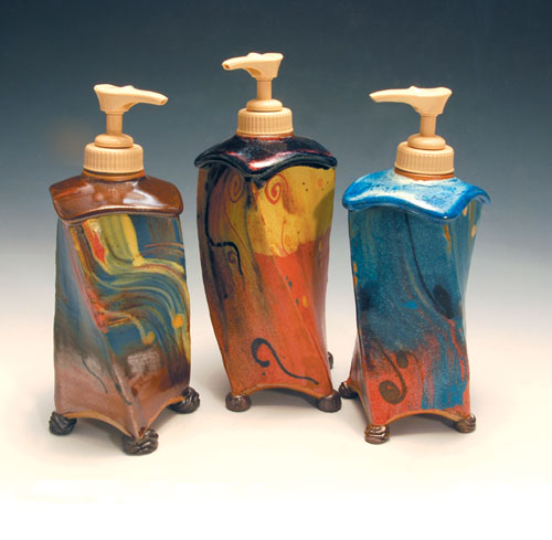 Three finished lotion dispensers, 7 in. (18 cm) in height, handbuilt using extruded parts, with added feet of unglazed dark brown clay and multicolored slip-glazes. Pump dispensers added after glaze firing.