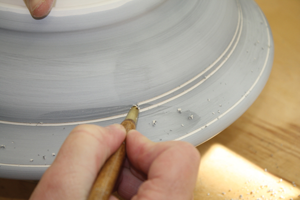 7 Carving concentric circles reminiscent of lines created in rippling water and that define banded areas around the rim.