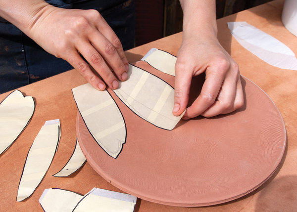 8 Sketch your desired shapes onto the stickers, then cut them out. Use the cut out shapes to create a composition, peel off the parchment paper backing, and affix the stickers to the plate’s surface.