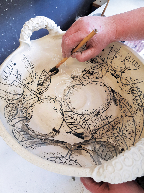 9 Clean the messy waxy bits off of the surface, then fill the carved outlines of the pattern with a dark colored underglaze.