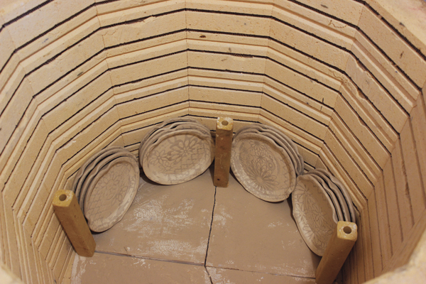 1 When loading work vertically in a bisque kiln, begin with the sturdiest plate or platter and place it in the kiln with the rim touching the kiln shelf. Make sure that the bottom of the foot rests against the wall in front of the elements but does not touch the elements. 