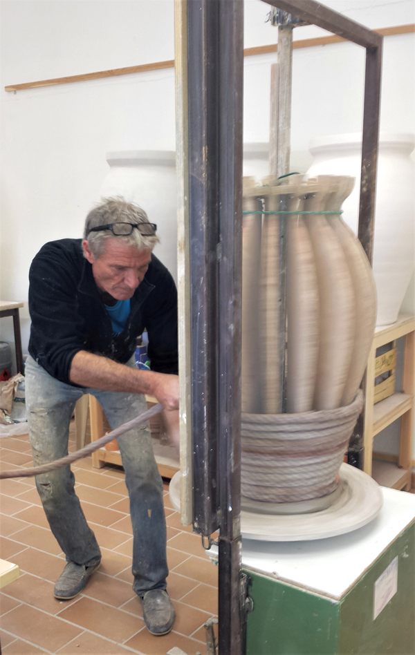 4 Coiling a thick rope around the wooden armature, starting at the slab base of the jar on the wheel head and working toward the top.