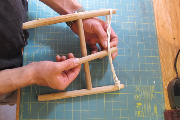 8 Insert the shorter wooden dowel into the middle of the tensioning rope and rotating the dowel to create tension.