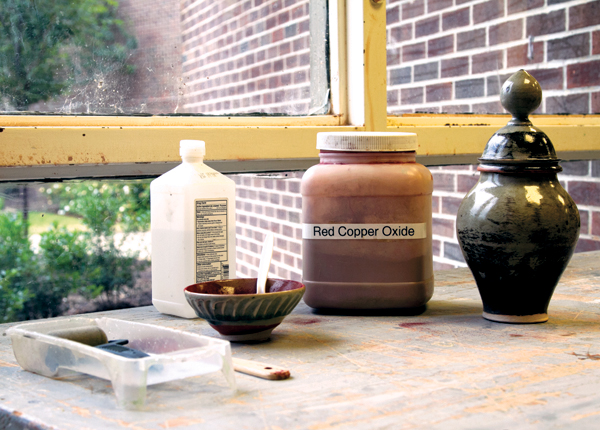 3 Supplies needed for oxide fusion printing (organized from left to right): a small paint roller and tray, isopropyl alcohol, a mixing container, the chosen oxide (red copper oxide), and a ceramic piece.s