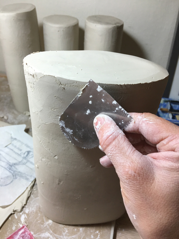 2 After scoring the bottom edge of the cylinder and the corresponding area on the slab, attach the bottom piece, shave down the sides with a serrated rib tool, then with the smooth rib tool.
