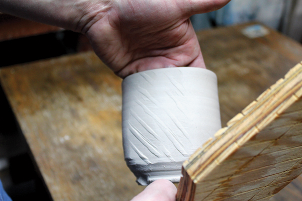 3 Place one hand on the inside of a leather-hard pot for support, then paddle the exterior of the pot to alter its surface.
