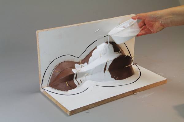 5 Begin pouring a thin coat of plaster over the clay model that will flow into and preserve any texture on the model and prevent bubbles and gaps in the surface of your mold.