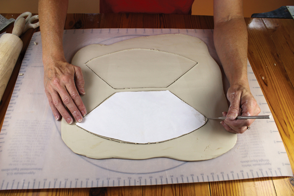 6 Line the mold with plastic wrap leaving the bottom hole uncovered, then tape the plastic to the outside of the mold. Roll out a slab, rib it smooth, place the template on the clay, and cut it out. Repeat this for a second cutout.