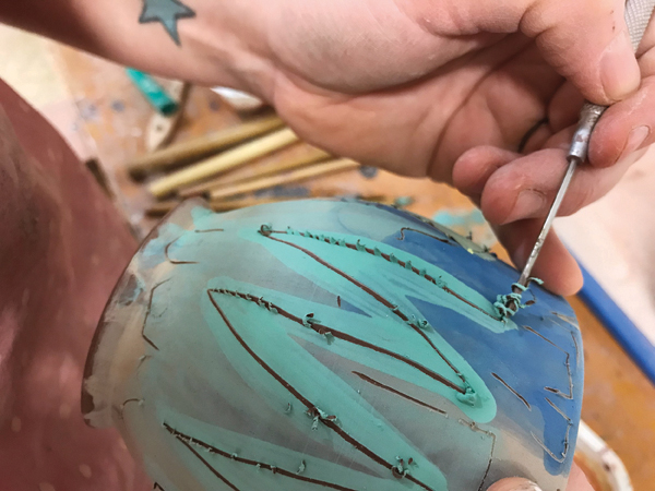 7 After the underglaze dries to the touch, I add detail with sgraffito decoration, drawing through the colors to reveal the clay.