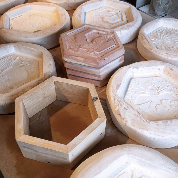 3 The hexagonal wooden template that is used to create the original clay paver models, plaster molds of the carved paver models, and several pavers that were made from clay and glaze waste.